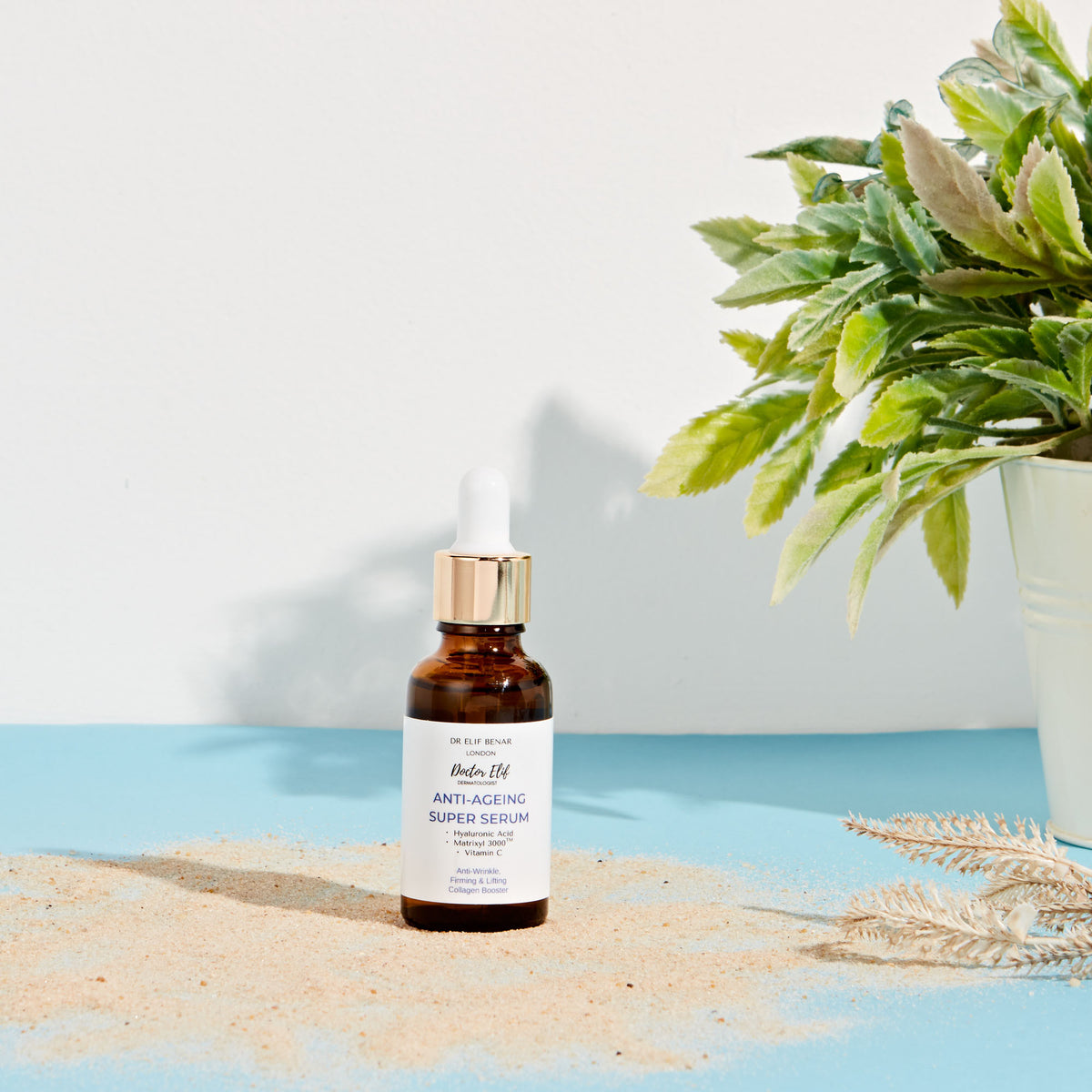 Dr Elif Benar Anti-Ageing Super Serum on sand with a green plant and summer sunlight